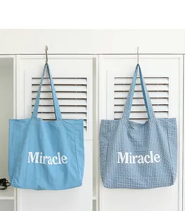 Detalle de bolsos tote de nailon azul lisos y de cuadros con estampado Miracle blanco.