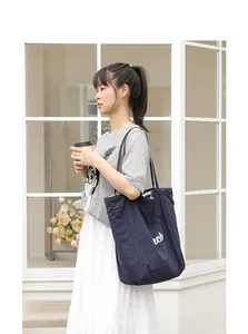 Vista lateral detallada del bolso tote de nailon azul marino con estampado de letras blancas