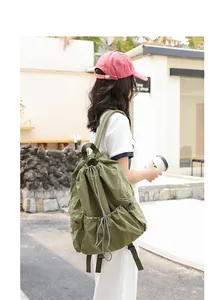Casual olive green nylon backpack with drawstring closure shown in outdoor lifestyle setting.