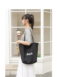 Imagen de detalle de un bolso tote de nailon negro con la palabra Beach impresa en blanco