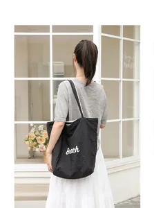 Vista trasera de una mujer con bolso tote de nailon negro e impreso 'Beach' blanco