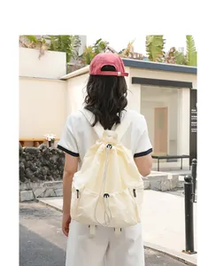 Back view of a creamy white nylon drawstring backpack worn by a model outdoors.