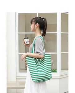 Green and white striped canvas tote bag carried by a model in a lifestyle scene