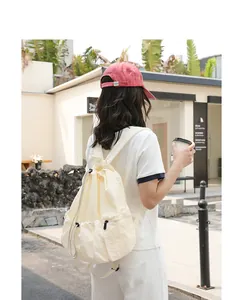 Outdoor lifestyle detail of a cream-colored drawstring nylon backpack with pleated texture.