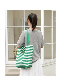 Detail view showing a large green and white striped canvas tote bag worn by a female model.