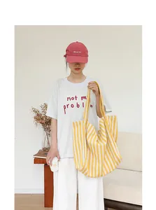 Bolso tote grande de lona con rayas amarillas y blancas llevado por una modelo joven