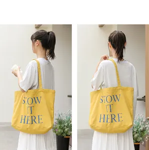 Vista posteriore della borsa tote in tela gialla con stampa lettere blu STOW IT HERE