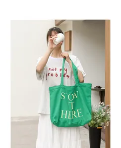 Vista dettagliata di una borsa tote in tela verde con stampa, tenuta da una modella