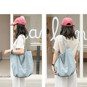 Detail view of light blue nylon tote bag worn by a model in a casual street setting.