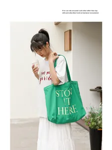 Borsa tote in tela verde con scritte gialle indossata da una modella all'aperto.
