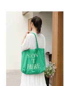 Vista posteriore di una borsa tote in tela verde con la scritta artistica STOW IT HERE