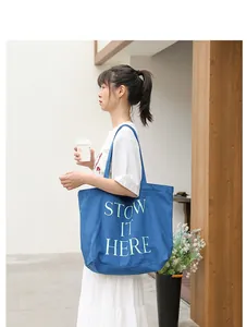 Elegante borsa tote in tela blu con stampa STOW IT HERE indossata da una modella