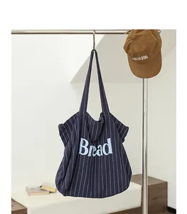 Stylish navy blue striped canvas tote bag with 'Bread' letter print hanging on a rack
