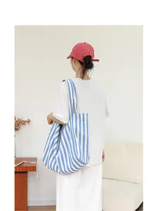 Bolso tote grande de lona con rayas azules y blancas llevado por una modelo en un interior