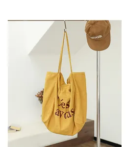 Sac cabas minimaliste en lin jaune avec imprimé lettrage élégant suspendu au support.