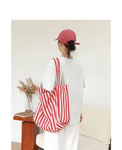 Bolso tote de lona a rayas rojas y blancas llevado por modelo en el hombro, vista detallada.