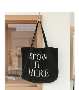 Vista dettagliata di una borsa tote in tela nera con stampa di lettere bianche STOW IT HERE