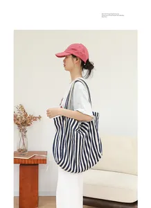 Modelo mostrando el perfil lateral de un bolso tote grande de lona a rayas azules