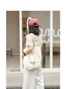 Woman carrying a large beige nylon tote bag with black letter print detail