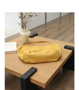 Sac fourre-tout en lin jaune avec imprimé lettre posé sur une table basse en bois moderne.