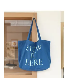Dettaglio di una borsa tote in tela blu con stampa STOW IT HERE in un ambiente interno accogliente