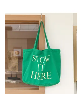 Borsa tote in tela verde vivace con scritta 'STOW IT HERE' stampata in un contesto casa