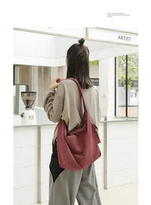 Detail view of a burgundy checked canvas messenger bag with a knotted strap worn by a model.