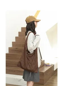 Side profile view of a large brown suede shoulder bag with elegant drawstring detail