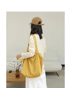 Back view of a model carrying a mustard yellow corduroy drawstring tote bag