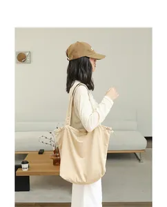 Detailed side view of a model carrying a large beige pleated suede drawstring tote bag