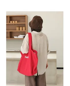 Detail of a bright red linen tote bag with 'Salé' print worn by a model in a minimalist setting