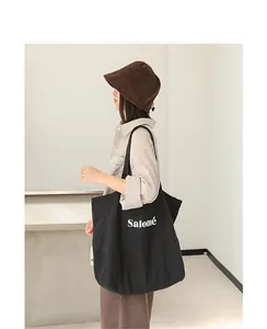 Detailed side view of black canvas tote bag with Salomé print on model wearing hat