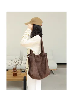 Close-up of brown suede drawstring tote bag worn on shoulder in a minimalist setting