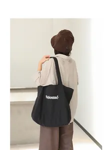 Artistic black canvas tote bag with white Salomé letter print worn on shoulder detail