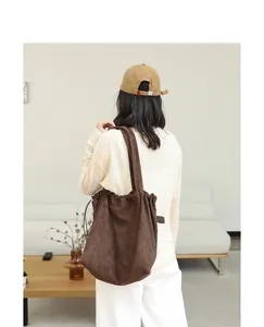 Detail view of a brown suede drawstring tote bag carried by a person in a minimalist room