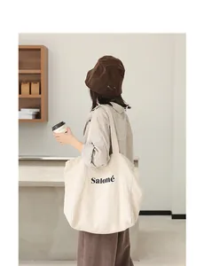 Back view of a woman carrying a large beige linen tote bag with Salomé print detail