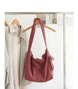 Detailed view of red plaid Japanese style messenger bag with knotted strap hanging on rack