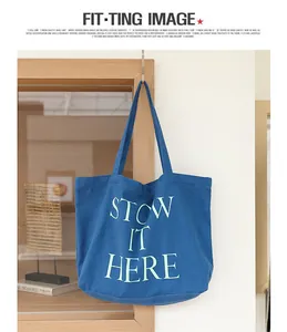 Primo piano della borsa tote in tela blu con la scritta STOW IT HERE vicino a una finestra.
