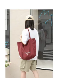 Detail shot of a burgundy nylon tote bag with Oufave Party embroidery in street scene