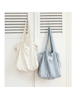 Dos bolsos tote de lona con lunares y cordón ajustable colgados en una puerta.