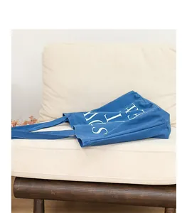 Primo piano di una borsa tote in tela blu con stampa di lettere su un divano.