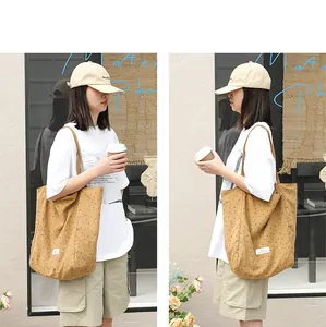Model carrying a khaki nylon tote bag with black polka dots in a casual street setting.