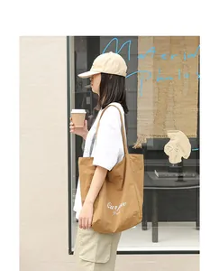 Casual artsy brown nylon tote bag with white letter print held by model in urban setting