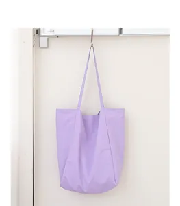 Bolso tote minimalista de nailon lila colgado de un gancho sobre pared blanca
