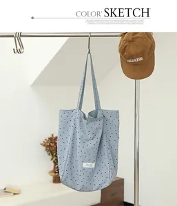 Detail view of a light blue nylon tote bag with black polka dots hanging in a studio