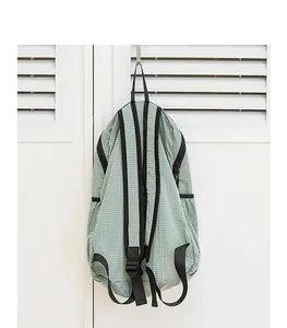 Close-up view of a minimalist light green checkered nylon backpack hanging on a white door.