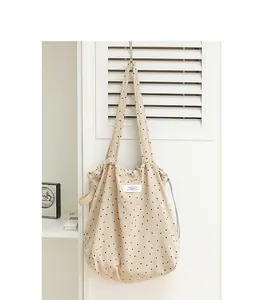 Primer plano de bolso tote de lona beige con lunares, cordón ajustable y asas largas