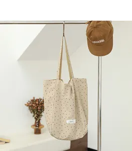 Detailed view of cream polka dot tote bag with minimalist white label and long straps.