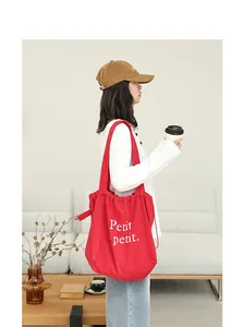 Bolso tote rojo de algodón y lino con cordón y letras impresas, llevado por una modelo.
