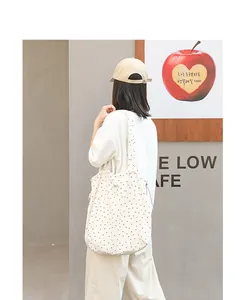 Model trägt eine stilvolle weiße Canvas-Tasche mit schwarzen Punkten in einem Café